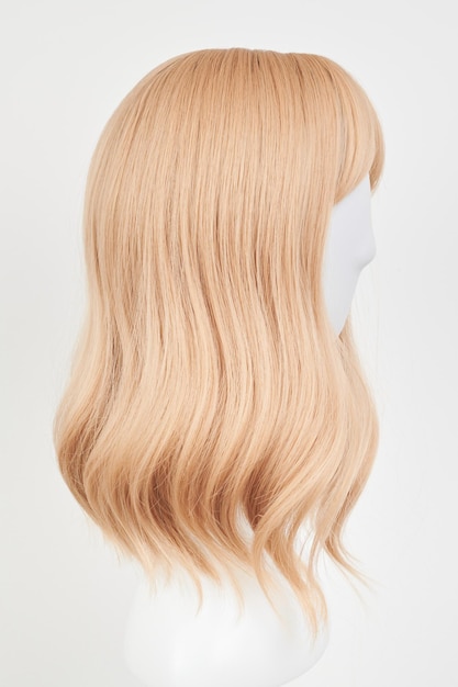 Natural looking blonde fair wig on white mannequin head Middle length hair cut on the plastic wig holder isolated on white background side view