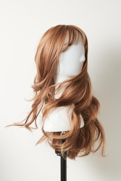 Natural looking dark blonde wig on white mannequin head Long fair hair cut on the plastic wig holder isolated on white background