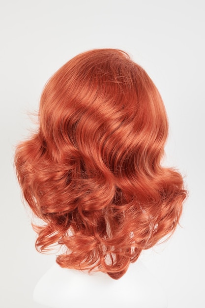 Natural looking ginger wig on white mannequin head Medium length hair with wavy curls on the plastic wig holder isolated on white background back view