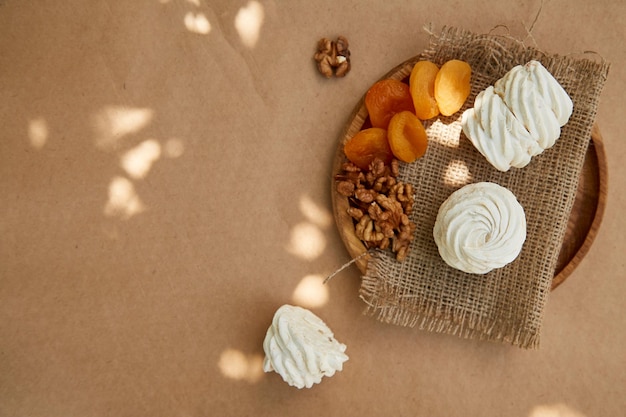 Natural marshmallows with dried apricots walnuts on wooden plate under sunlight and cup of tea Copy space Cozy garden
