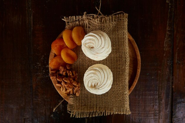 Natural marshmallows with taste of dried apricots walnuts on wooden plate and sacking Rustic background Top view