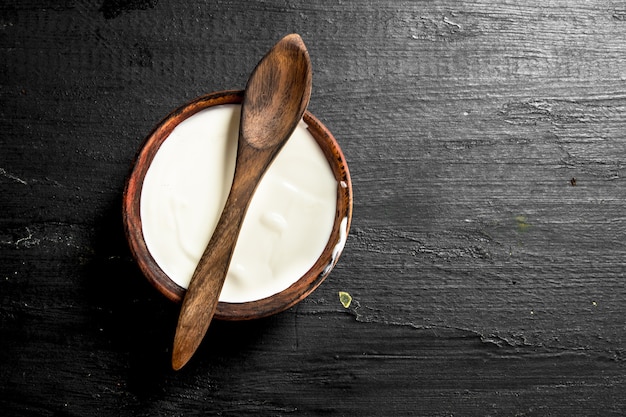 Natural milk yogurt in a bowl with a spoon. On the black chalkboard.