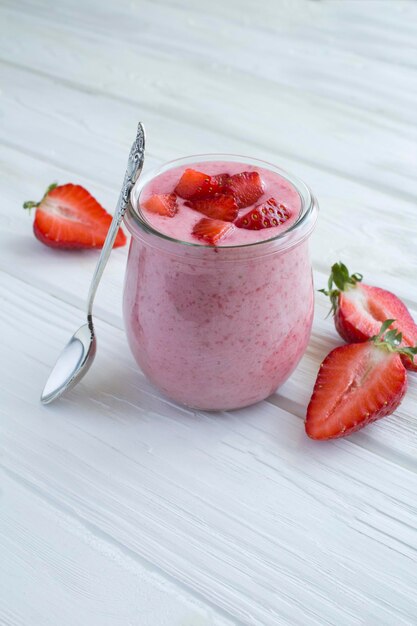 Natural milk yogurt with strawberry in the glass jar on the white wooden background Location vertical