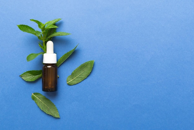 Natural Mint Essential Oil in a Glass Bottle organic cosmetics with herbal extracts of mint on colored background