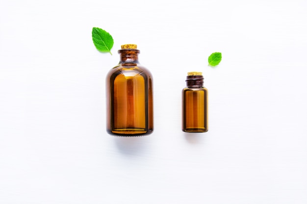Natural Mint Essential Oil in a Glass Bottle with Fresh Mint Leaves on white wooden background.