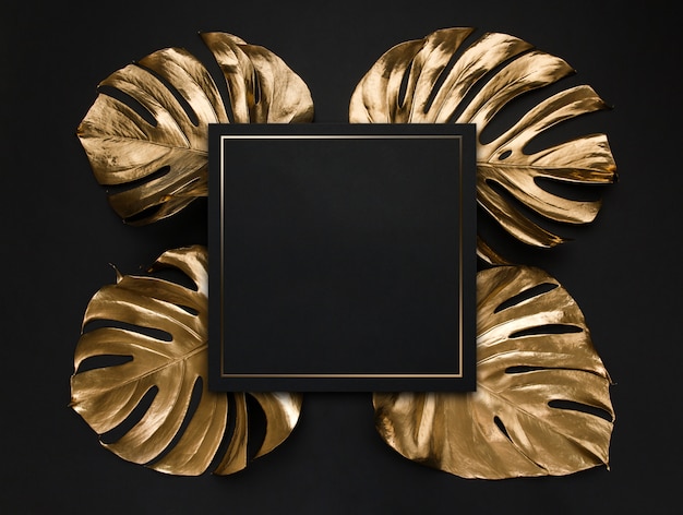 Photo natural monstera leaves spray painted with gold metallic paint and a black empty note