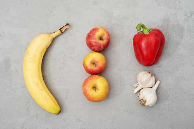 灰色のコンクリートの背景に自然に見える果物と野菜バナナアップルペッパーとニンニク生未加工食品とビタミン