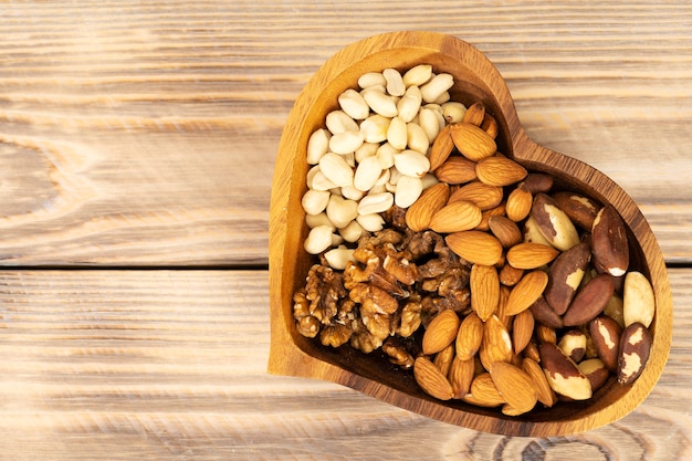 Natural nutritional blend of various nuts in a wooden plate in the shape of a heart symbol on a brown wooden table