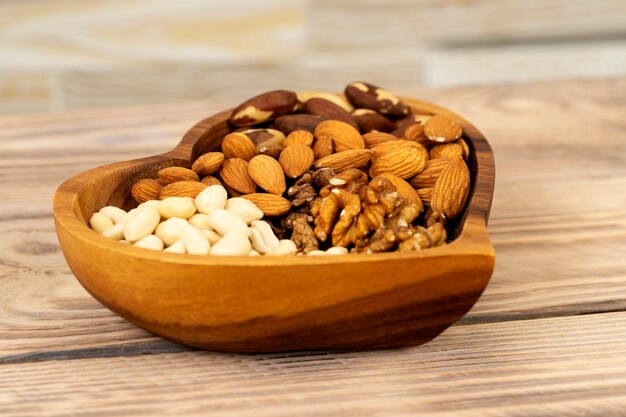 Natural nutritional blend of various nuts in a wooden plate in the shape of a heart symbol on a brown wooden table