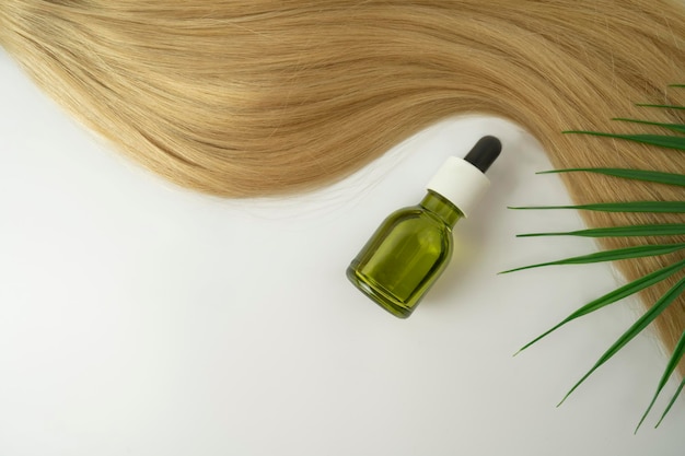 A natural oil or serum for hair care and a ply of blonde hair\
lying on a white background