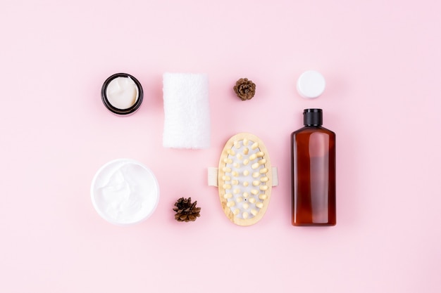 Natural organic beauty concept. Shampoo or cosmetic lotion bottle, towel, open cream jar, massager. Skin care products on pink surface. Creative body care layout. Beauty, spa flat lay.
