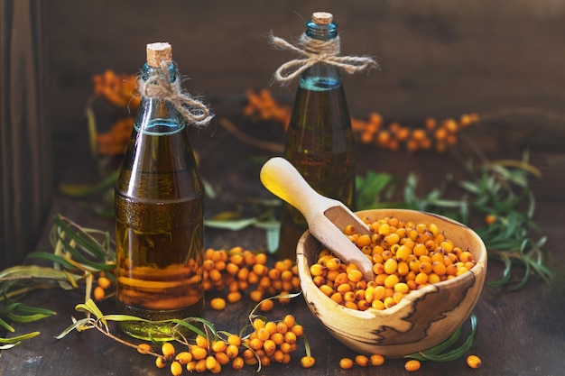 Natural organic seabuckthorn berry in bowl and sea buckthorn oil in glass vintage bottle on dark wooden background Dark rustic style natural remedy