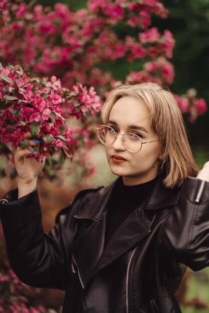 Natural portrait of a young happy blonde girl in black on the\
backdrop of red flower tree in autumn