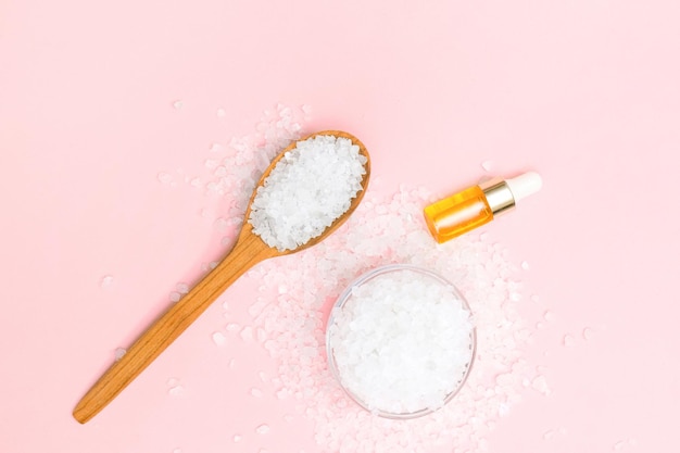 Natural sea salt in glass bowl and wooden spoon isolated on beige pink background.