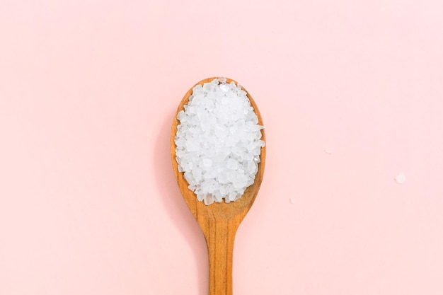 Natural sea salt in a wooden spoon isolated on a beige pink background.