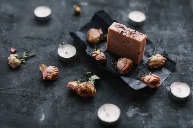 Natural soap and rose flowers on dark surface