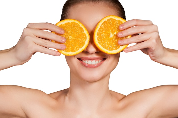 Natural spa. Beautiful young shirtless woman holding pieces of orange in front of her eyes while standing isolated on white background