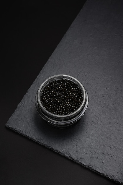 Natural sturgeon black caviar in a glass jar on a slate plate  national dish of Russian cuisine