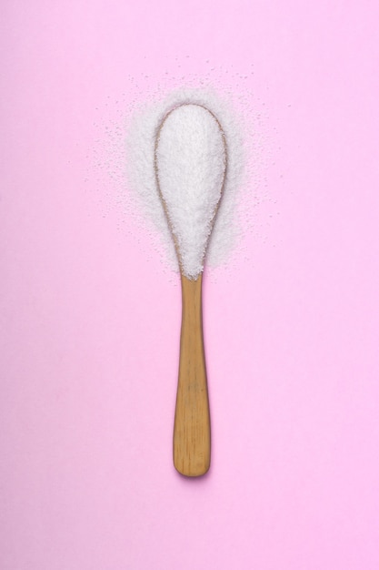 Natural sweetener poured into a wooden spoon on a pink background