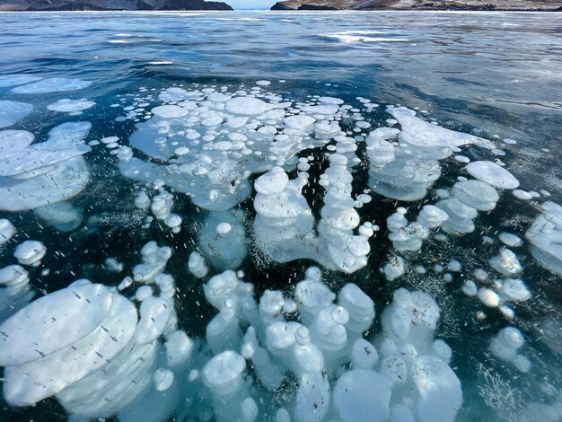 凍った湖に白い泡とひびが入った冬の氷の自然な風合い 凍ったバイカル湖の表面に氷とひびが入った抽象的な背景