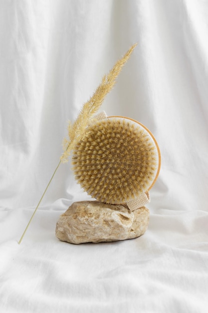 Natural wooden body brush with papas grass balancing on rocks white background Massage relax spa