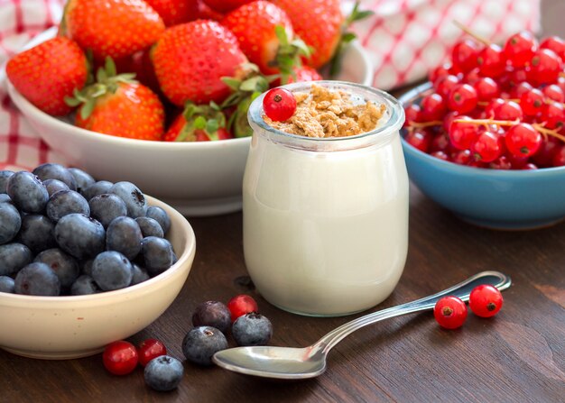 Natural yogurt, fresh berries and granola on a wooden table close up. Healthy breakfast concept