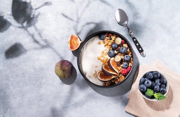 写真 影のある青い背景にボウルにグラノーラベリーとイチジクを入れたナチュラルヨーグルト健康的で栄養価の高い朝食