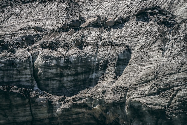 Nature background with icefall near glacier with cracks and scratches. Natural backdrop with icy wall and moraines. Beautiful landscape with shiny glacial wall and stones in sunlight. Glacier texture.