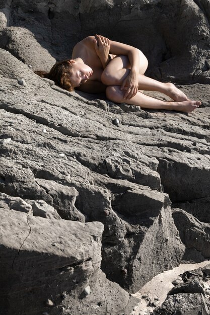 Nature, beauty, youth and healthy lifestyle concept. Naked woman on a sandstone. Nude girl on beach. Young naked woman sitting on clay cliff on seashore