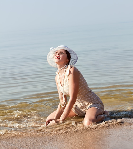自然、美しさ、若さと健康的なライフスタイルのコンセプト。海に対して白い傘と白い帽子とストライプのレトロな水着の女性