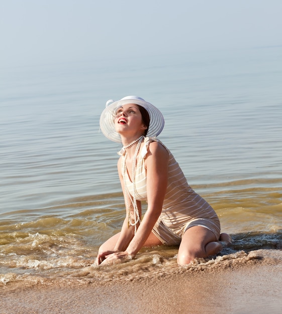 Nature, beauty, youth and healthy lifestyle concept. Woman in a striped retro bathing suit with a white umbrella and white hat against the sea