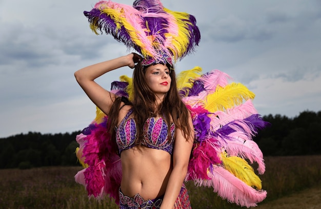 Nature, beauty, youth and healthy lifestyle concept. Young woman in bright colorful carnival costume posing outdoors.