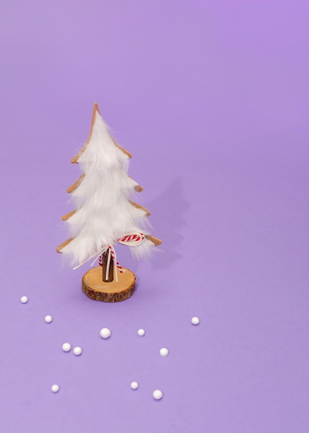 Nature hand-made white christmas tree decorated with white fur. white textile and wooden material. small decorative snowballs and red ribbon rope. pastel purple background.