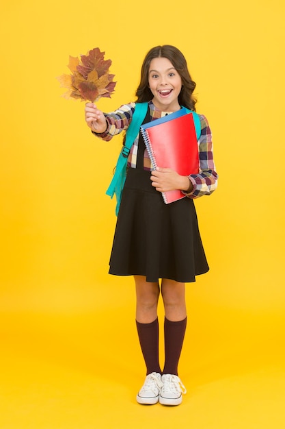 Nature lesson Happy little child hold autumn leaves for biology lesson Small girl smiling with lesson books and yellow foliage Lesson can be entertaining Back to school