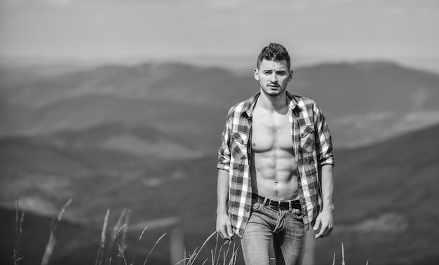 Nature lover sexy macho man in checkered shirt cowboy in hat outdoor countryside concept farmer on rancho man on mountain landscape camping and hiking travelling adventure hipster fashion