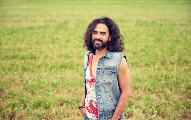 Foto concetto di natura, estate, cultura giovanile e persone - sorridente giovane hippie in giubbotto di jeans su campo verde