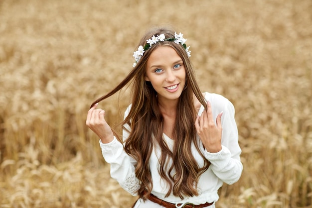 nature, summer, youth culture and people concept - smiling young hippie woman wearing flower wreath on cereal field