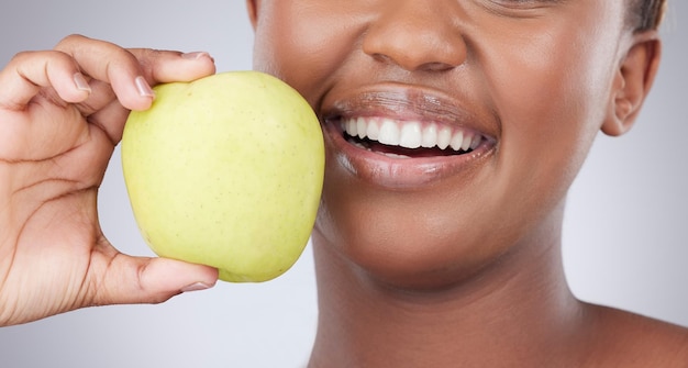 ネイチャーズ歯磨き粉。灰色の背景にリンゴでポーズをとる魅力的な若い女性のスタジオショット。