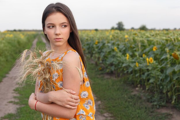 Natuur portret. Close-up van mooie vrouw in jurk houdt tarweoogst in haar handen terwijl ze in een geel tarweveld staat.