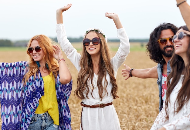 natuur, zomer, jeugdcultuur en mensenconcept - gelukkige jonge hippievrienden dansen op graanveld