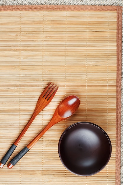 Natuurlijk houten bord, lepel en vork op een bamboerug.