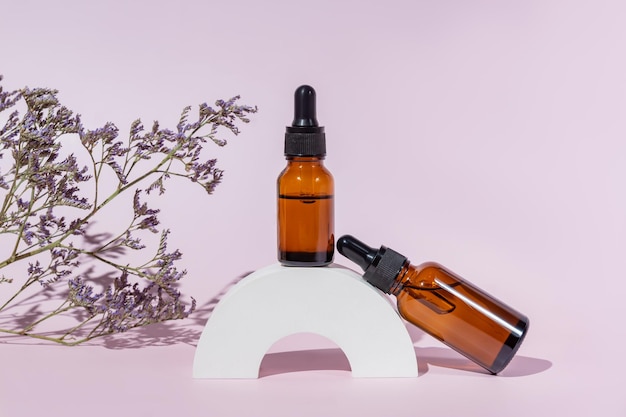 Natuurlijk huidverzorgingsproduct in glazen fles druppelaar vloeistof of serum voor vrouw gezichtshuid kruiden minerale cosmetica op witte betonnen standaard donker glas pakket cosmetologie minimalisme