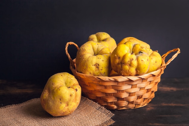 Natuurlijk kweepeerfruit met gebreken in een mand op een juteservet en een donkere houten achtergrond.