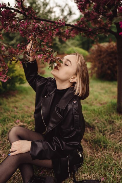 Natuurlijk portret van een jong gelukkig blond meisje in het zwart op de achtergrond van een roze bloemboom in de herfst