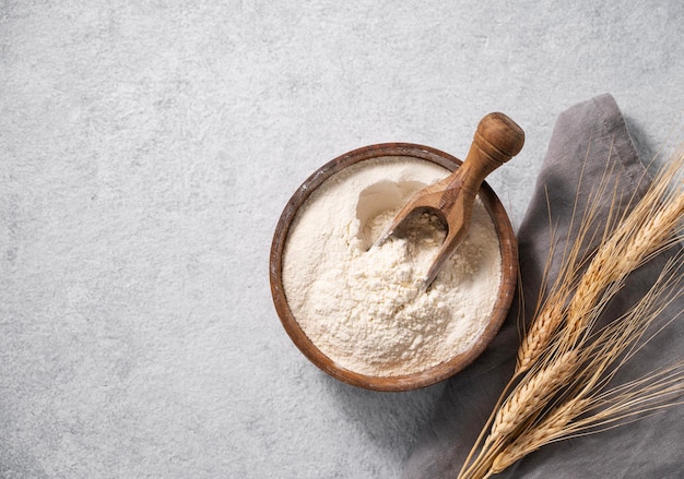 Natuurlijk tarwemeel in een houten kom op een blauwe achtergrond met takken van tarwe Het concept van een biologisch product voor thuis bakken