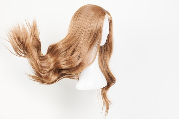 Natuurlijk uitziende donkerblonde pruik op het hoofd van de witte mannequin. Lang blond haar geknipt op de plastic pruikhouder geïsoleerd op een witte achtergrond