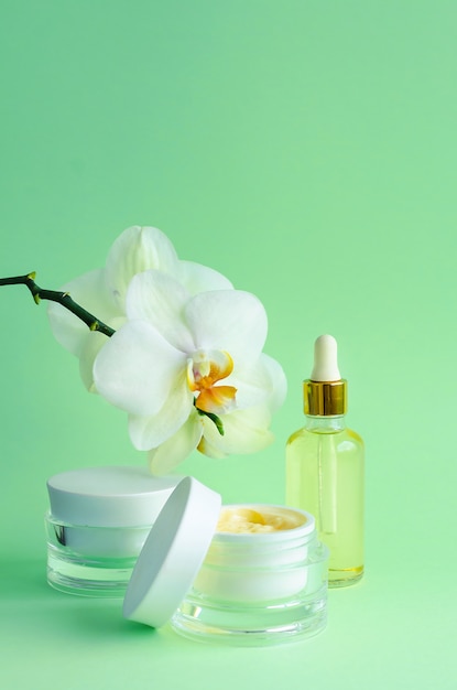 Natuurlijke anti-aging, voor jeugdcosmetica. crème, masker in pot, serum, vloeistof, olie in fles voor gezichtsverzorging, met orchideeën op groene muur. verticaal, patroon, kopieer ruimte