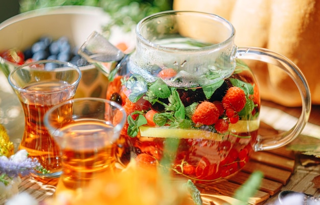 Natuurlijke aromatische fruitthee in een transparante theepot en in een kopje tussen bessen en bloemen Verwarmende aromatische thee met een diep aroma van bessen en wilde bloemen