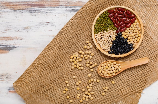 Natuurlijke biologische peulvruchten als sojabonen, rode, zwarte, groene en witte bonen gerangschikt op mooie cirkel houten dienblad en luxe lepel op placemat van keukentafel. Fruitkorrels bereid voor vitaminedessert.