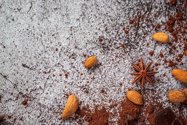 Natuurlijke cacaopoeder chocolade steranijs rauwe amandelen verspreid over een grijze betonnen achtergrond